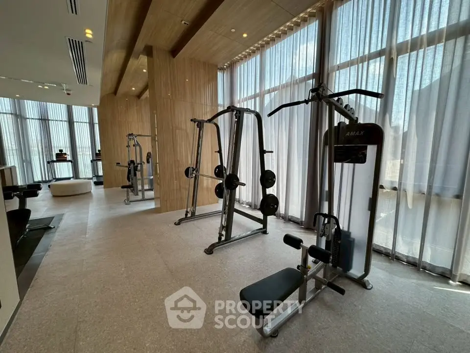 Spacious modern gym with natural light and state-of-the-art equipment in luxury building.