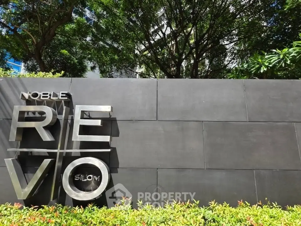 Modern building entrance with sleek signage and lush greenery at Noble Revo Silom.