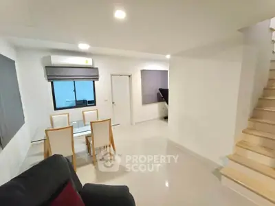 Modern living room with dining area and staircase in a bright, minimalist home interior.