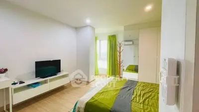Modern bedroom with green accents and sleek furniture, featuring a wall-mounted TV and ample natural light.