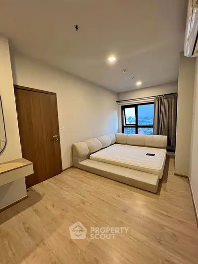 Spacious bedroom with large window and modern furnishings in a high-rise apartment.
