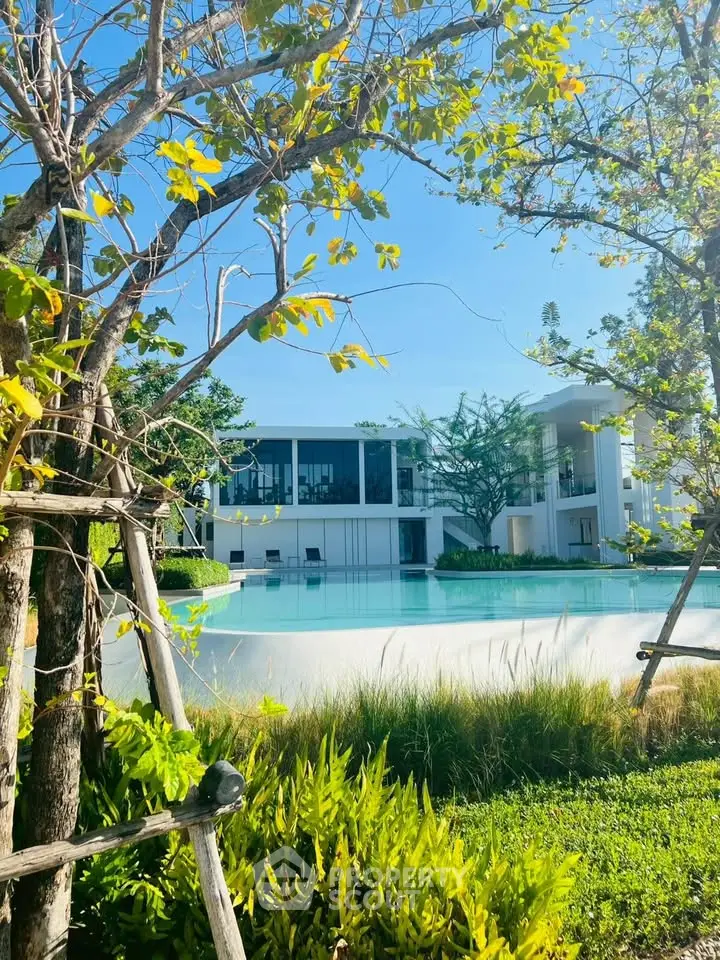 Luxurious modern building with serene pool and lush greenery, perfect for tranquil living.