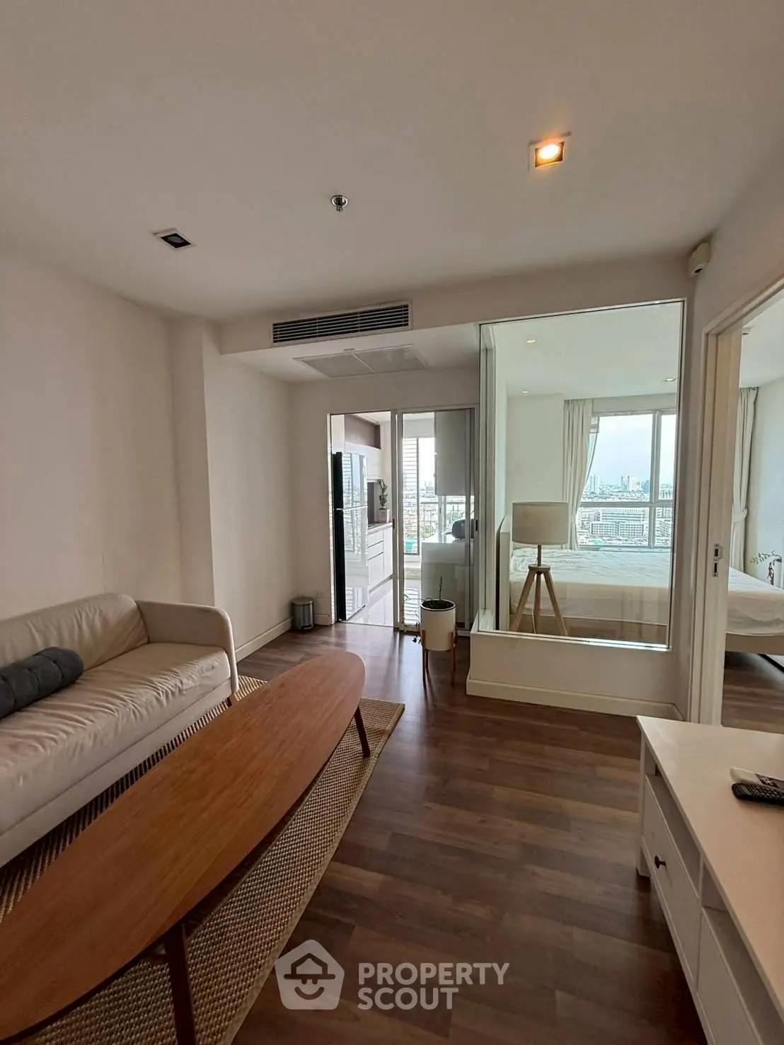 Modern living room with wooden flooring and cozy furniture, offering a glimpse into a stylish bedroom.