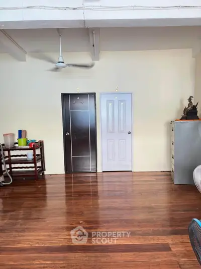 Spacious room with wooden flooring and minimalist decor, featuring two doors and a ceiling fan.