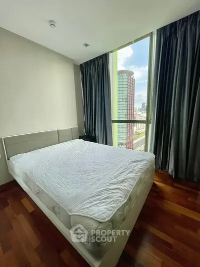 Spacious bedroom with large window offering stunning city view and natural light.