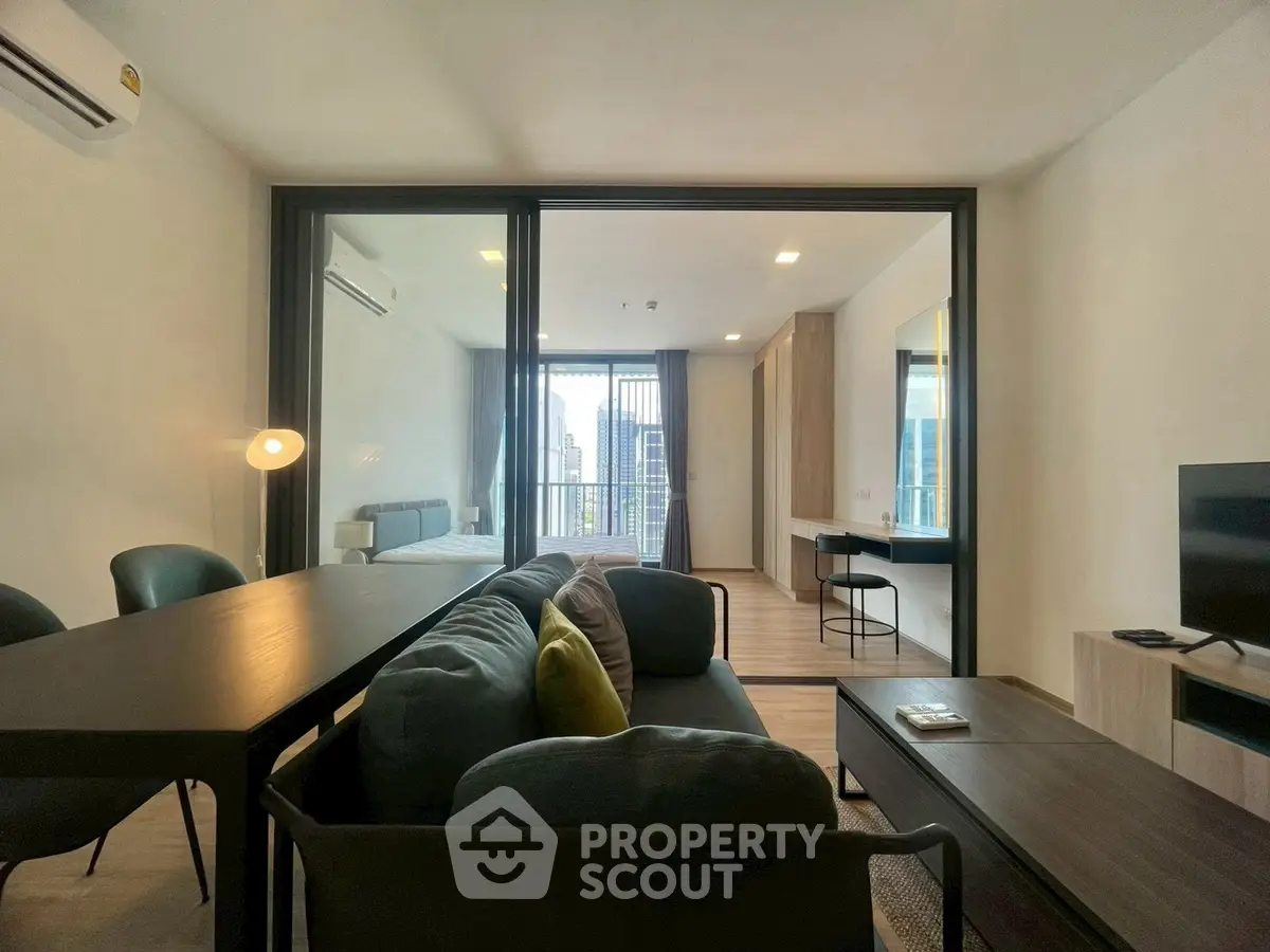 Modern open-plan living room with city view, featuring sleek furniture and glass partition to bedroom.