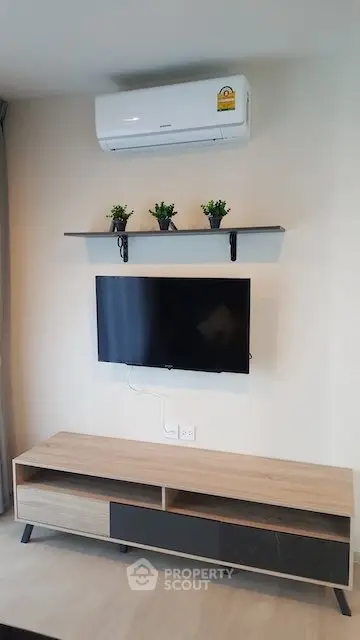 Modern living room with wall-mounted TV and air conditioner, stylish shelf with plants, and sleek media console.