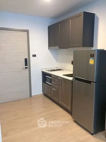 Modern compact kitchen with sleek cabinets and stainless steel fridge in a stylish apartment.