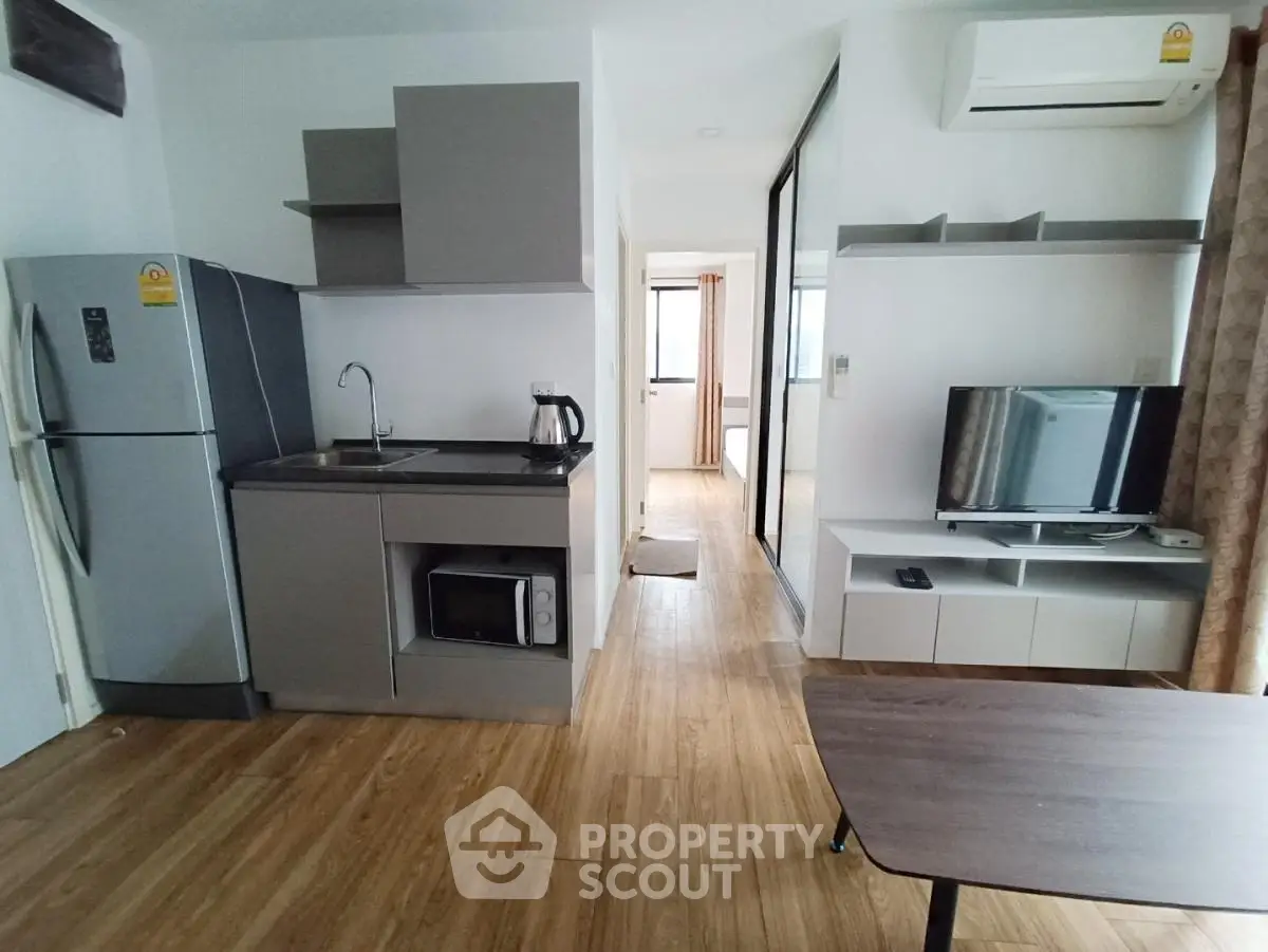 Modern apartment interior with kitchen and living area, featuring sleek appliances and wooden flooring.