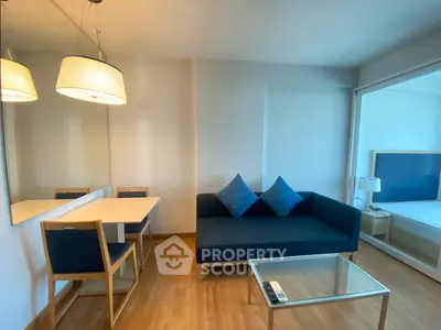 Modern living room with blue sofa, glass coffee table, and dining area in a cozy apartment.