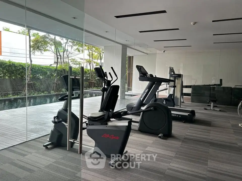 Modern gym with state-of-the-art equipment and pool view in luxury residential complex.