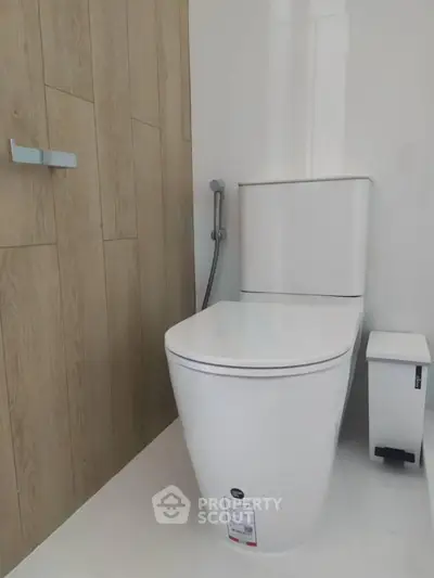 Modern bathroom with sleek toilet and wooden accent wall, perfect for contemporary homes.