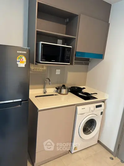 Modern compact kitchen with appliances including fridge, microwave, and washing machine.