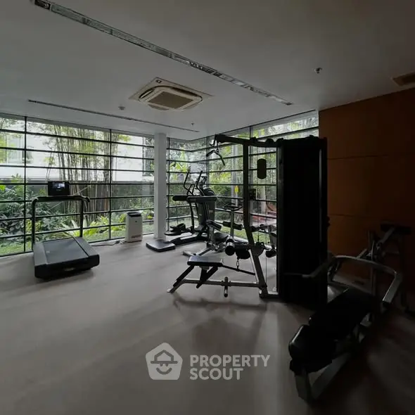 Modern gym with large windows and fitness equipment in a serene setting.