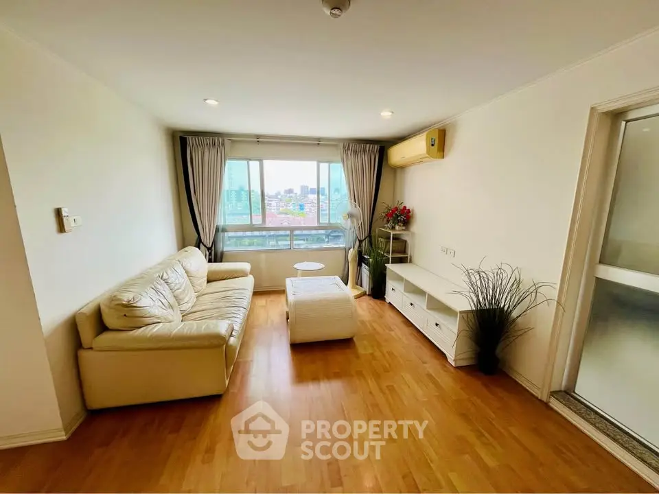 Spacious living room with wooden flooring, cozy sofa, and large window offering city views.