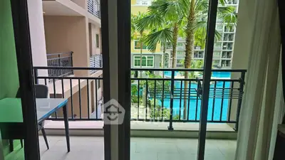 Charming balcony view overlooking a lush garden and sparkling pool in a modern apartment complex.