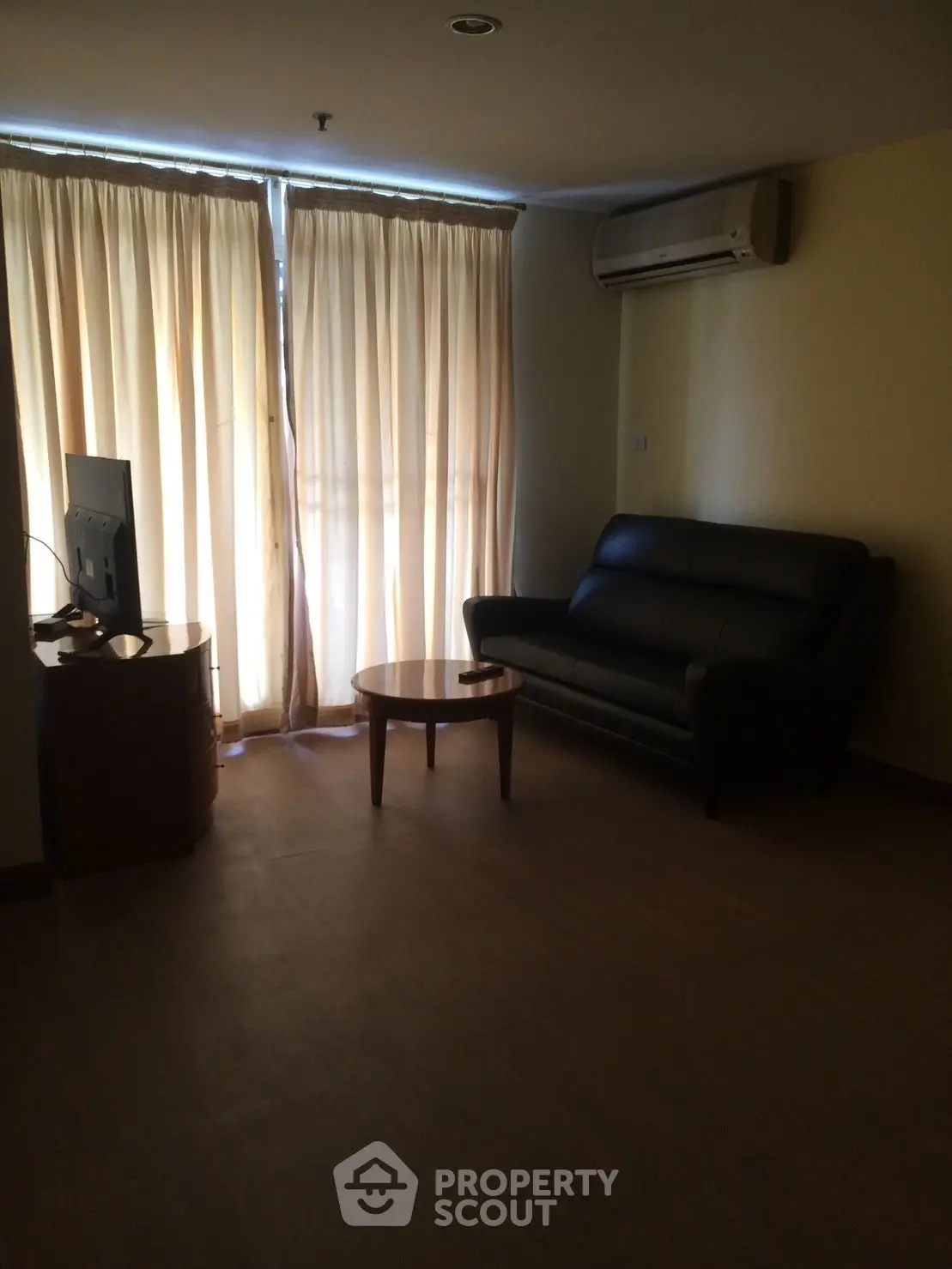 Cozy living room with sofa, TV, and air conditioning, featuring natural light through curtains.