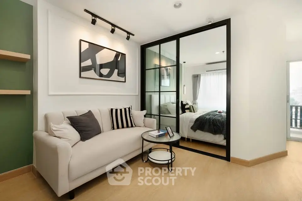 Modern living room with stylish decor and cozy sofa adjacent to a bedroom with glass partition.