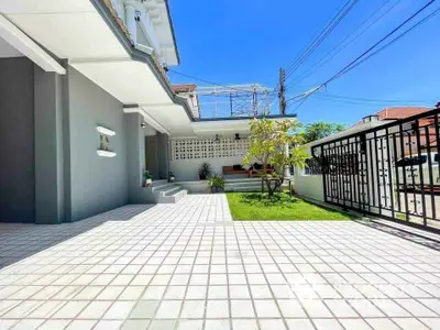 Modern home exterior with spacious tiled patio and lush garden area under clear blue sky.