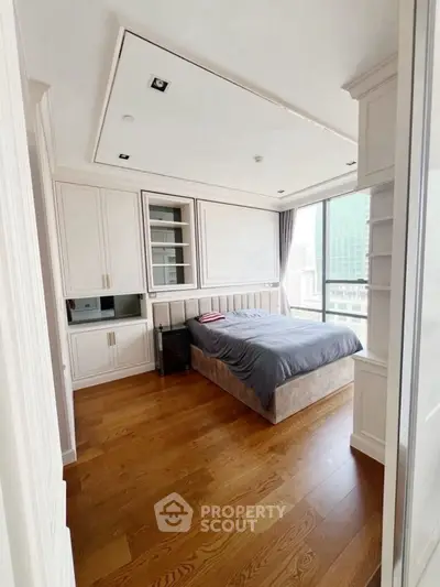 Modern bedroom with large window and built-in storage in high-rise apartment.