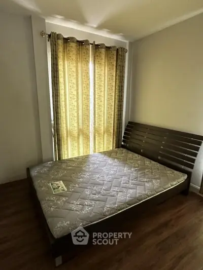 Cozy bedroom with wooden flooring and natural light through elegant curtains.