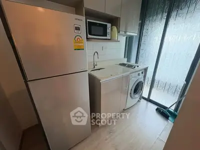 Modern kitchen with fridge, microwave, and washing machine in compact layout.