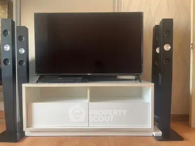 Modern living room setup with sleek TV and stylish speakers on wooden floor.