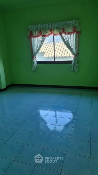 Spacious room with green walls and tiled floor, featuring a window with decorative curtains.