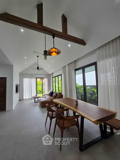 Spacious modern living room with high ceilings and elegant wooden beams, featuring large windows and stylish furniture.