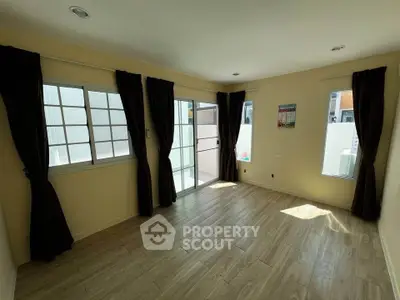 Spacious sunlit room with large windows and elegant curtains, perfect for versatile living space.