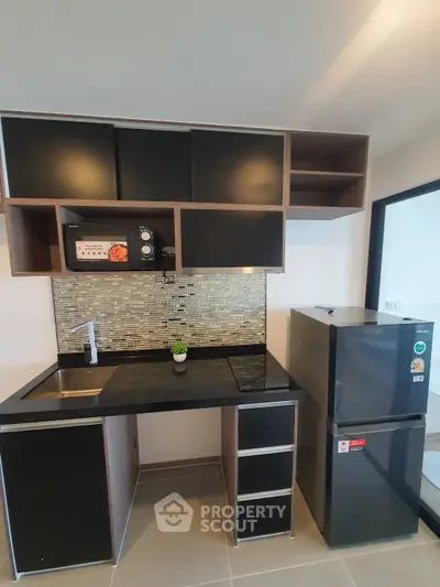 Modern kitchen with sleek black cabinets and compact fridge