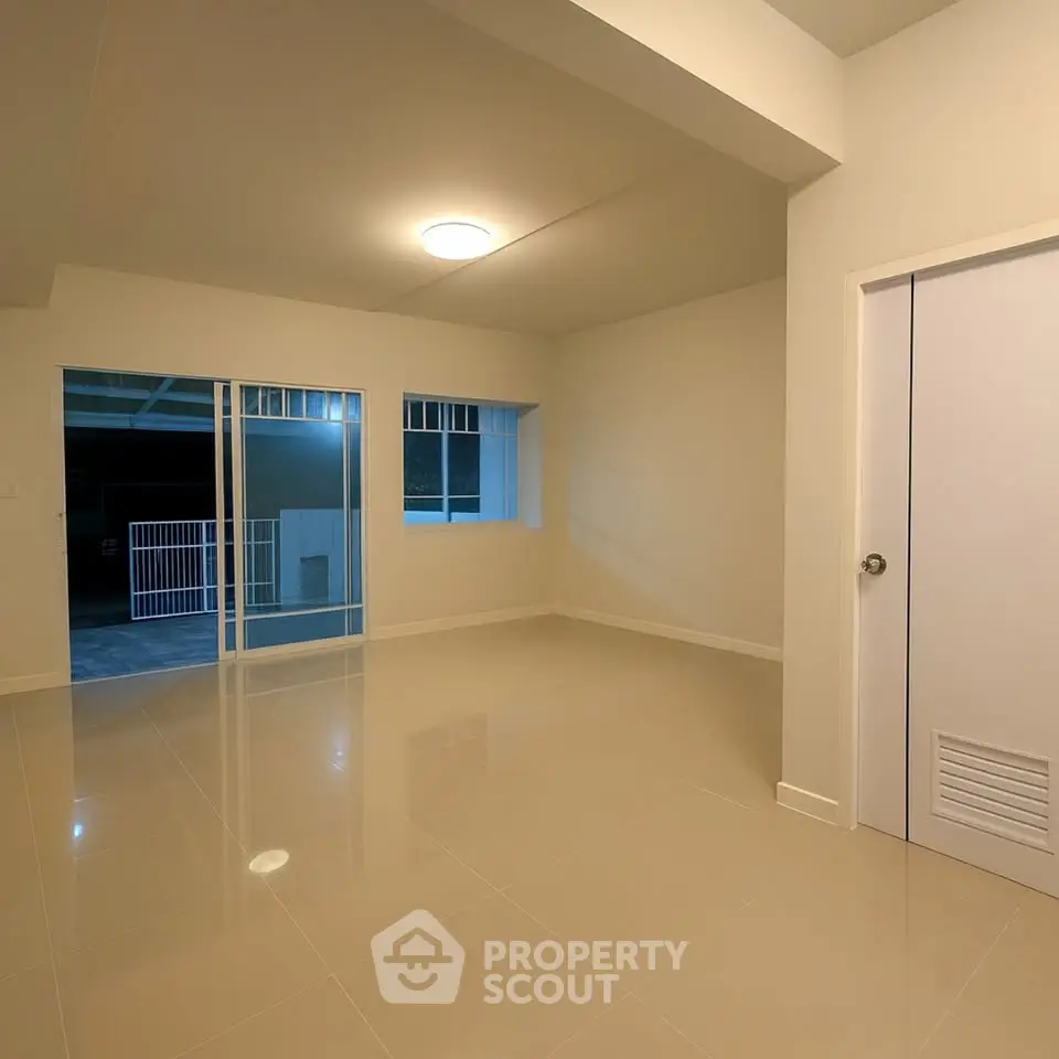 Spacious empty room with glossy tiled floor and sliding glass doors.