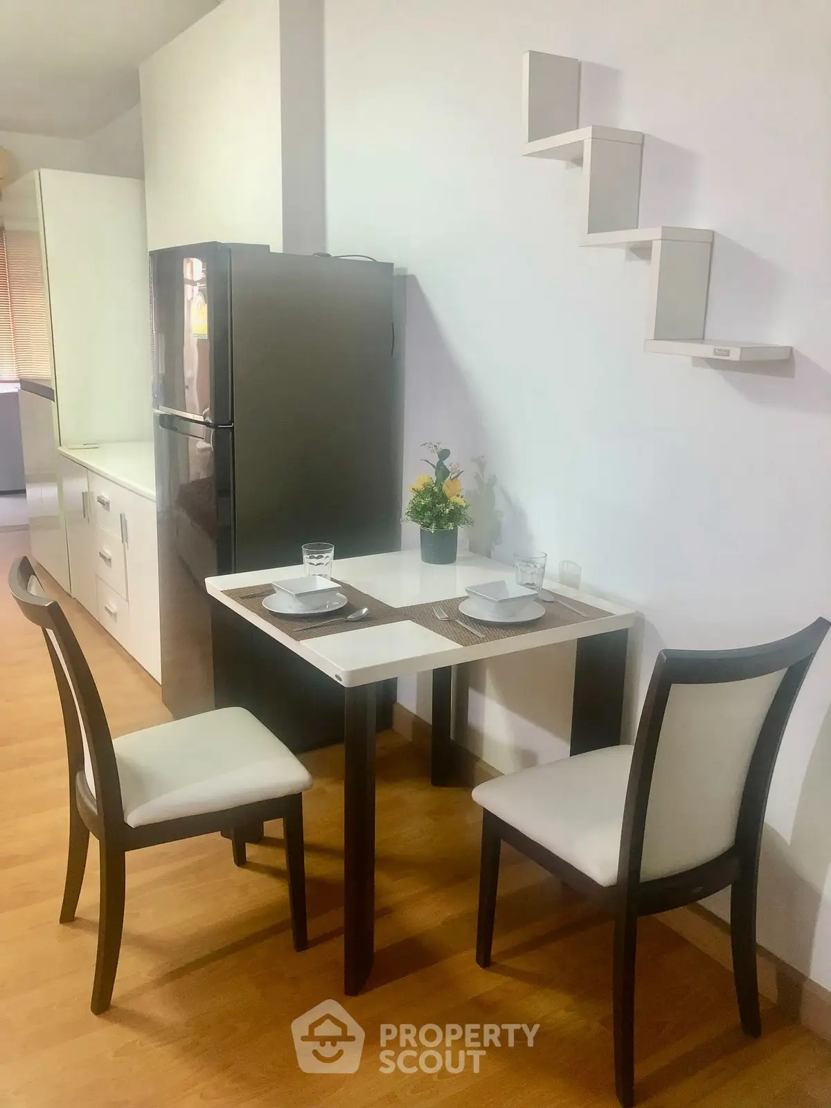 Charming dining area with modern table and chairs, adjacent to sleek kitchen with fridge, perfect for cozy meals.