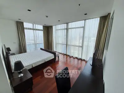 Spacious bedroom with floor-to-ceiling windows and city view, featuring hardwood floors and modern furnishings.