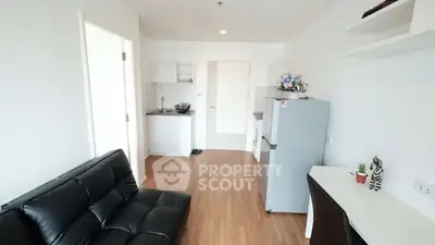 Modern studio apartment with sleek black sofa and compact kitchen area.