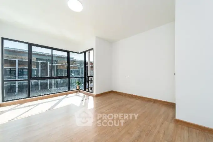 Spacious empty room with large windows and wooden flooring, ideal for customization.