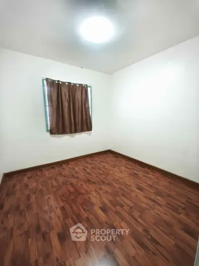 Spacious empty room with wooden flooring and a window, perfect for customization.
