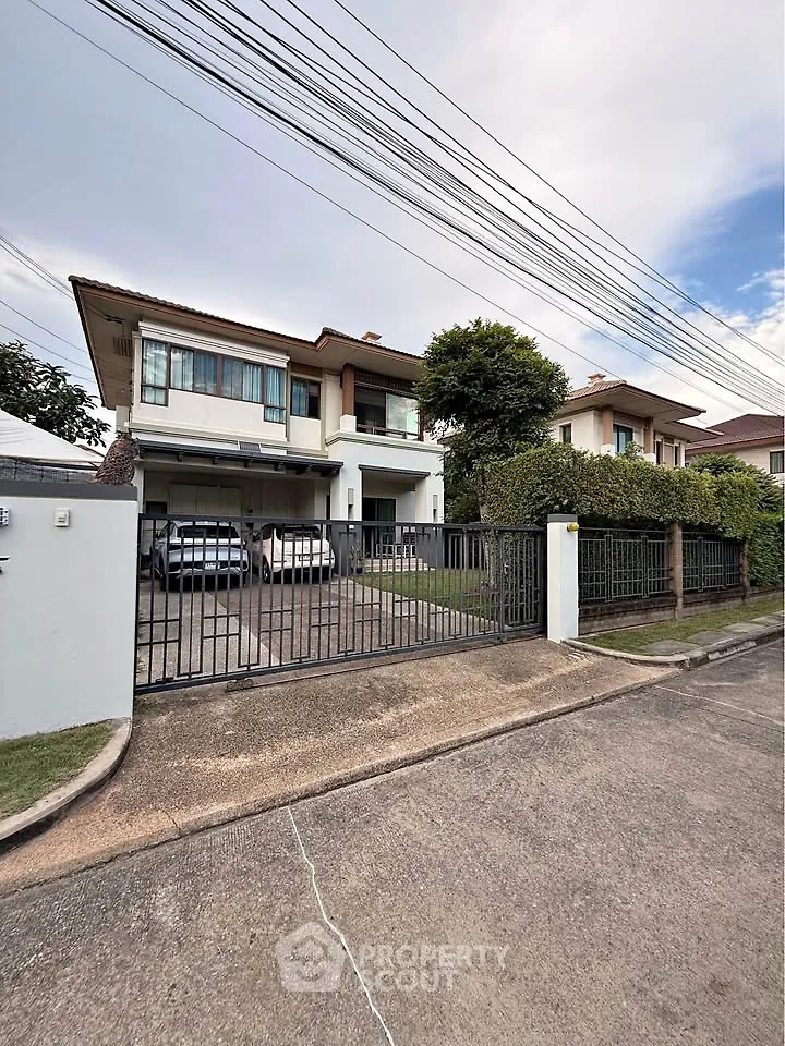 Spacious two-story house with a gated driveway and lush greenery in a serene neighborhood.