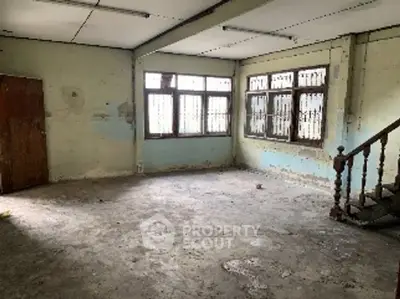 Spacious fixer-upper room with potential for renovation, featuring large windows and staircase.