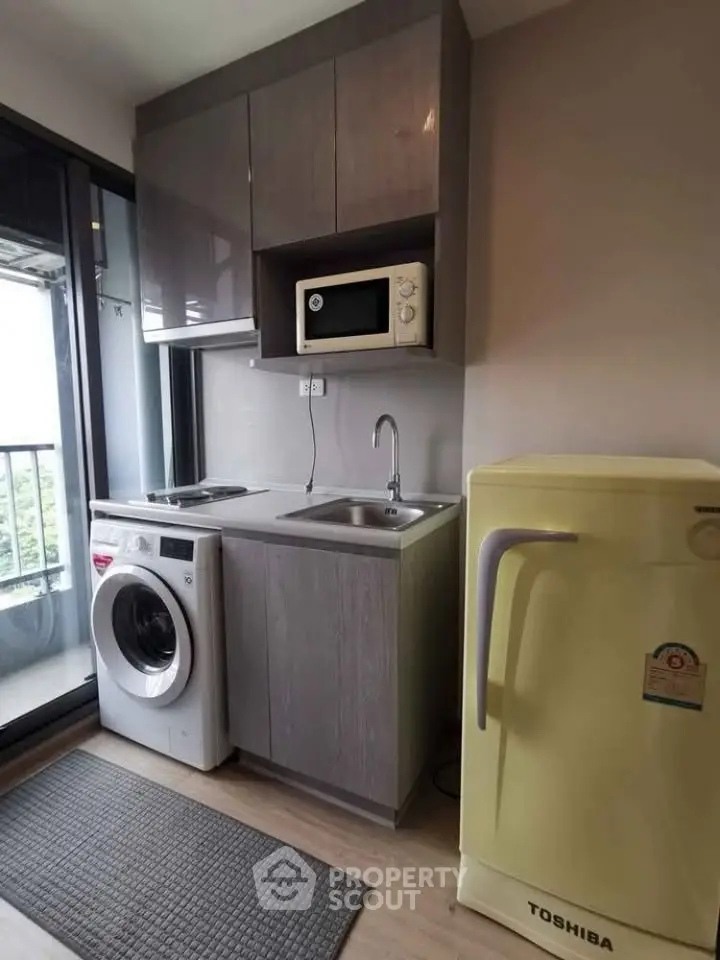 Compact kitchen with washing machine, microwave, and fridge in modern apartment.