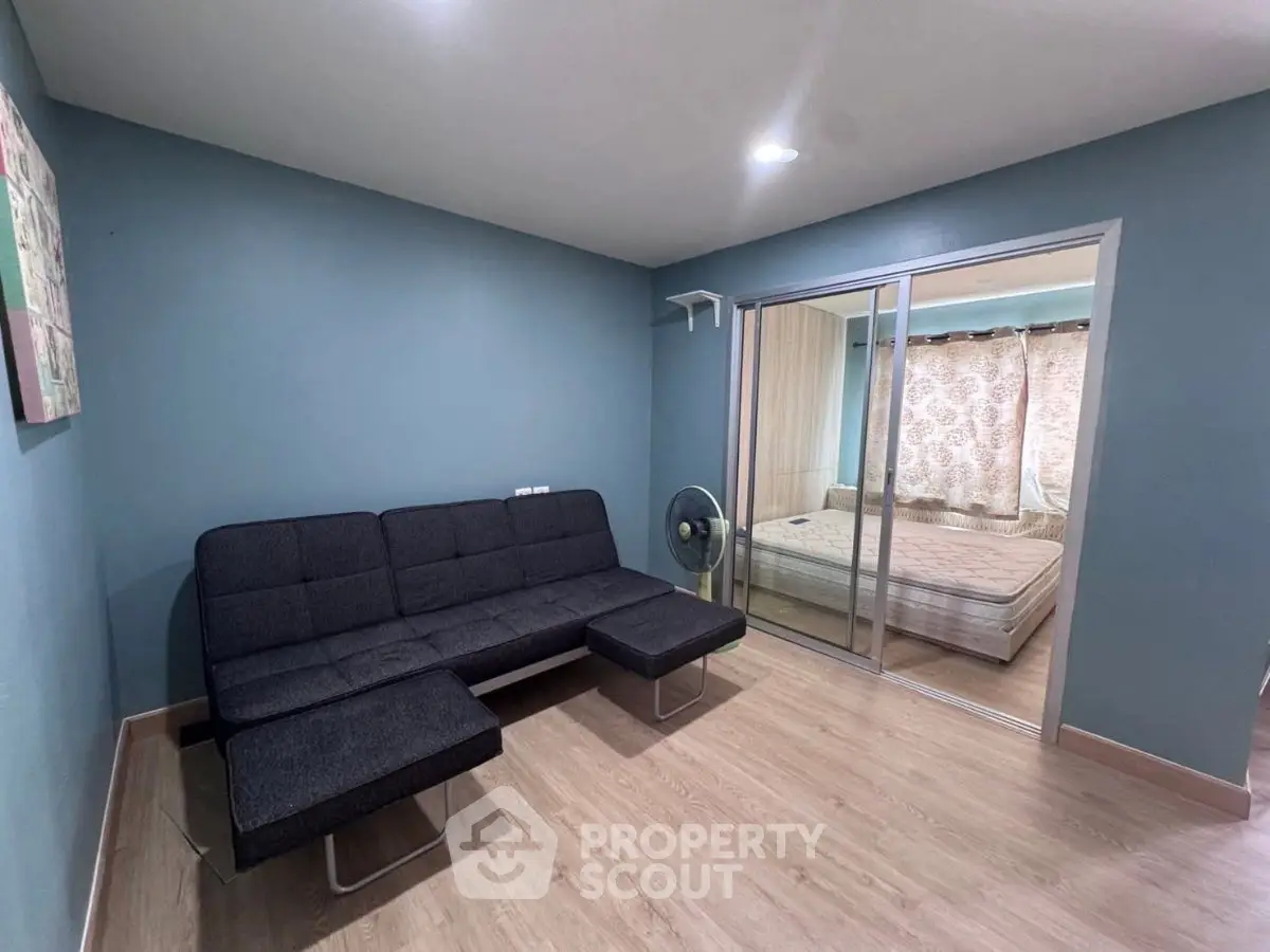 Modern living room with sleek black sofa and sliding glass doors leading to a cozy bedroom.