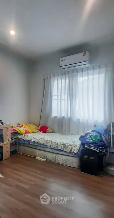 Cozy bedroom with natural light and wooden flooring, featuring a single bed and air conditioning.