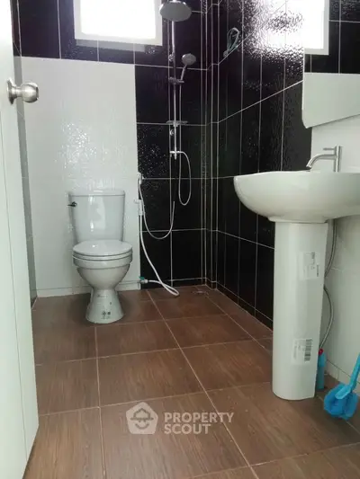 Modern bathroom with sleek black and white tiles, featuring a shower, toilet, and pedestal sink.