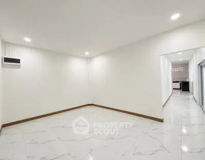 Spacious empty room with marble flooring and recessed lighting, leading to a modern kitchen.