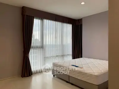 Spacious bedroom with large window and elegant curtains in modern apartment.