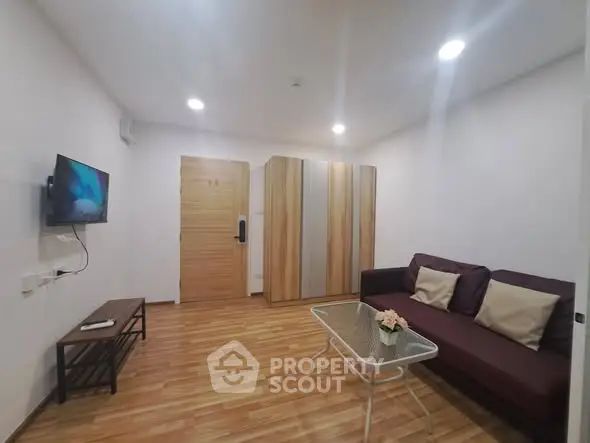 Modern living room with sleek wooden flooring, cozy sofa, and wall-mounted TV in a stylish apartment.