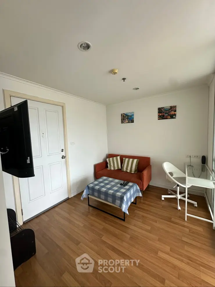 Cozy living room with wooden flooring, compact sofa, and modern desk setup.