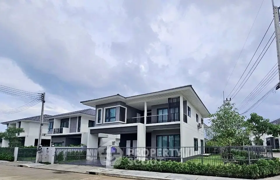 Modern two-story house with spacious balcony and lush garden in a serene neighborhood.
