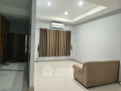 Spacious living room with modern lighting and sleek tile flooring, featuring a comfortable beige sofa and elegant curtains.