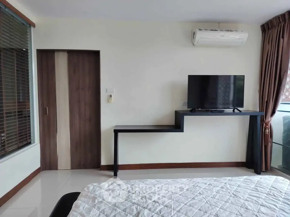 Modern bedroom with sleek TV setup and air conditioning, featuring a stylish design and natural light.